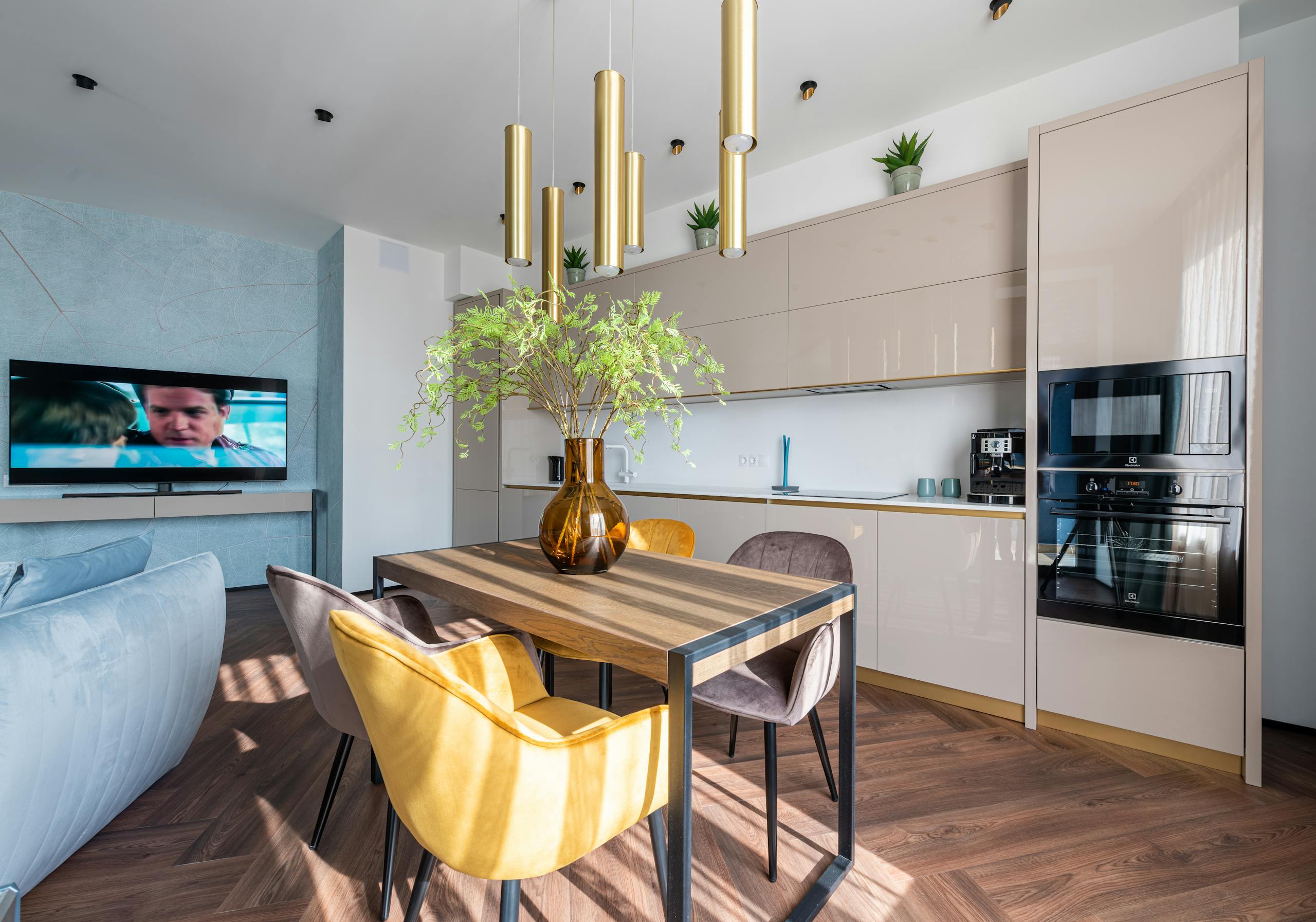 Contemporary kitchen interior with table and green flowers in glass vase in modern apartment with comfortable couch and TV set
